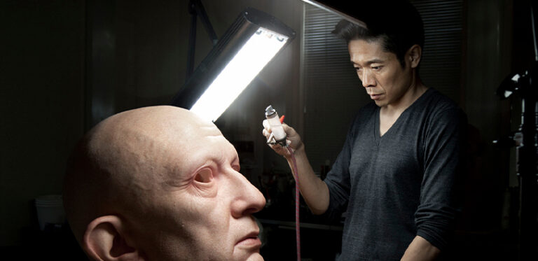 A photo of Kazu Hiro working on a model of a face.