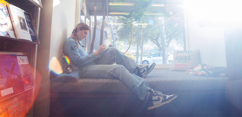 A photo of a student reading in the library window.