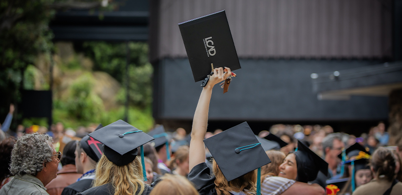 A photo of a student holding up their diploma at commencement.