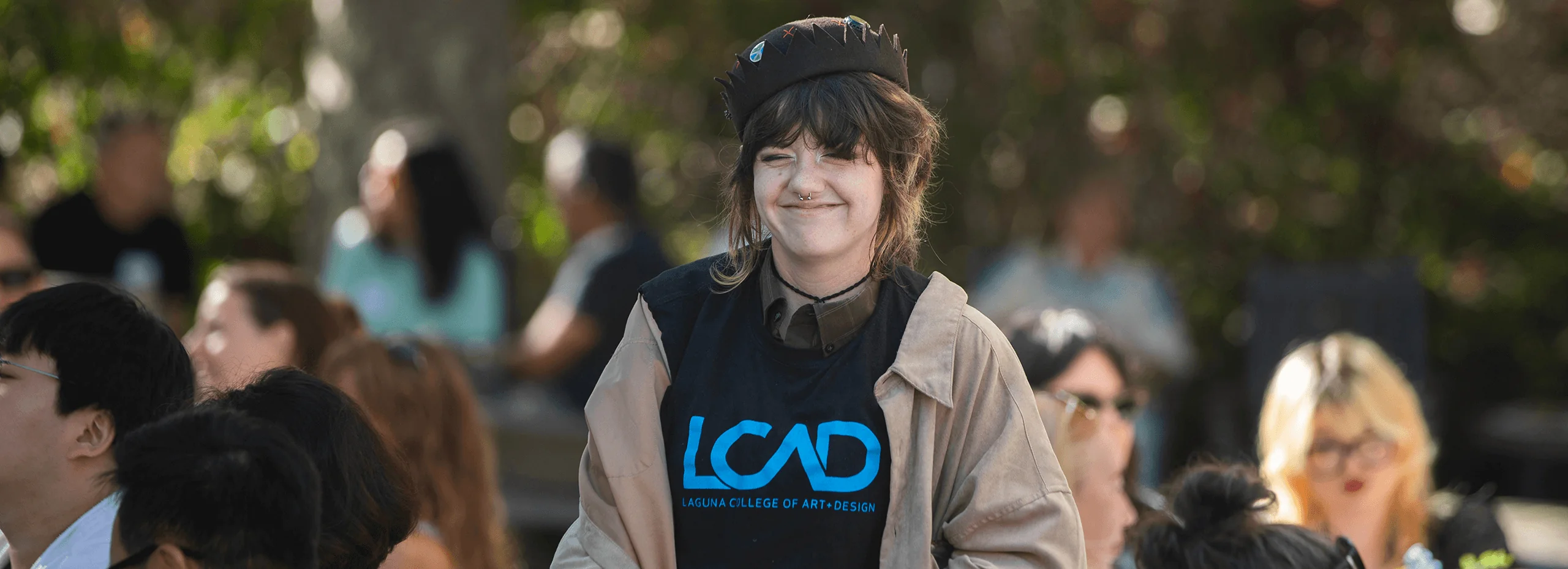 LCAD student smiling outdoors on campus in an LCAD shirt and tan jacket