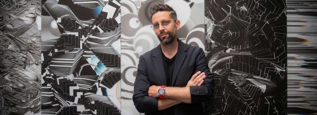 A photo of Mark Saville in front of black and white graphic artwork